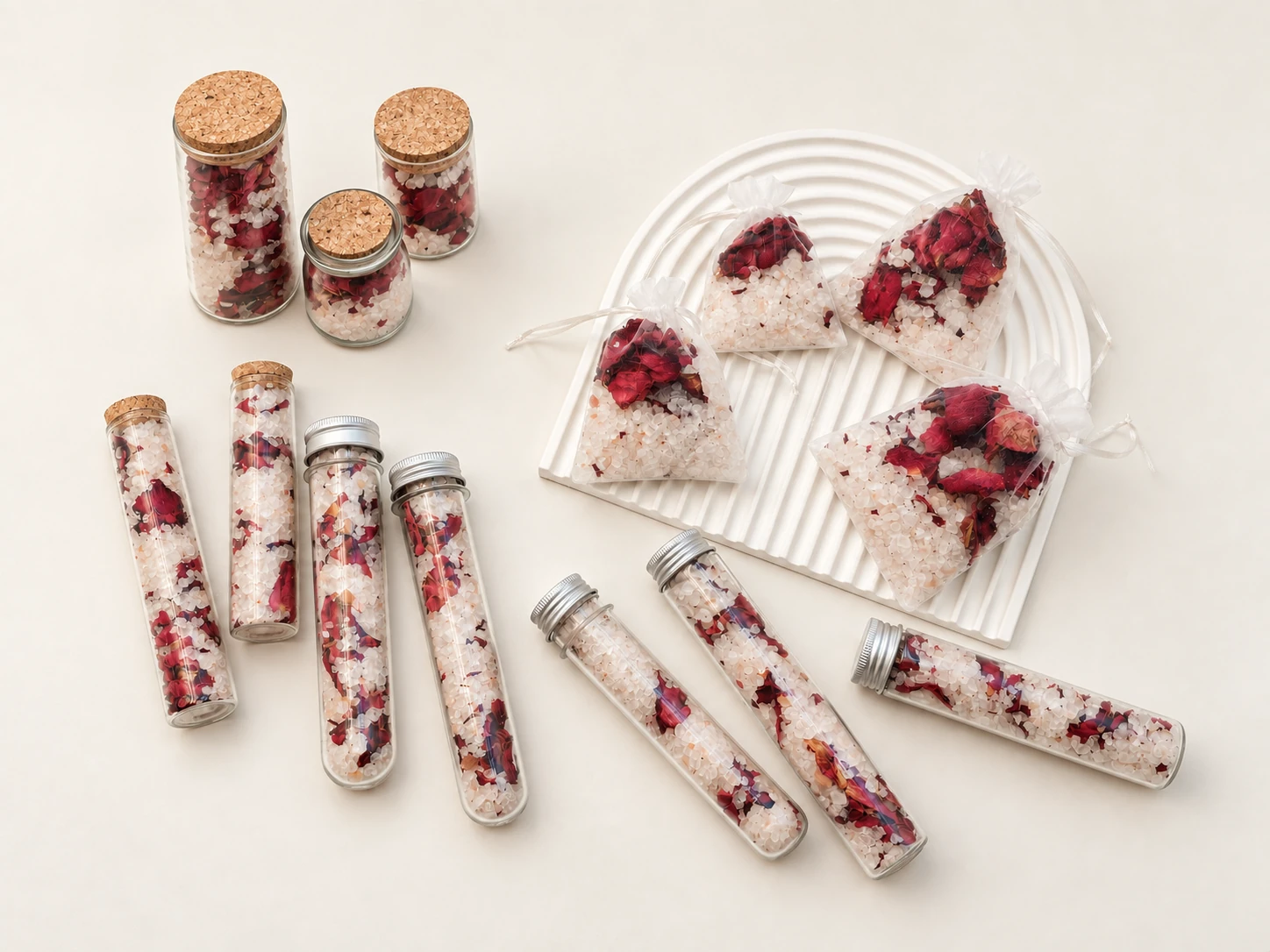Rose-petal bath blends in glass jars, tubes and drawstring sachets arranged on a white surface